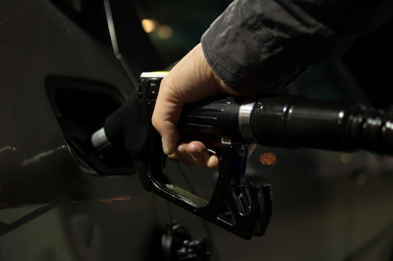 A hand holding a fuel nozzle at a vehicle's filler in low light